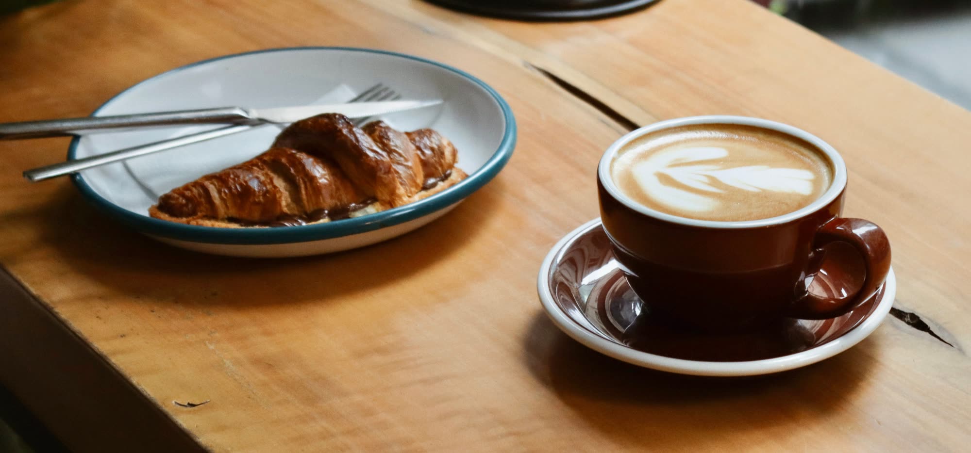 A croissant and a flat white on a wooden table
