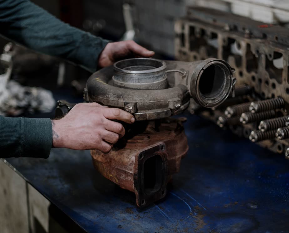 Hands turning a rebuilt turbocharger on a workbench next to a cylinder head