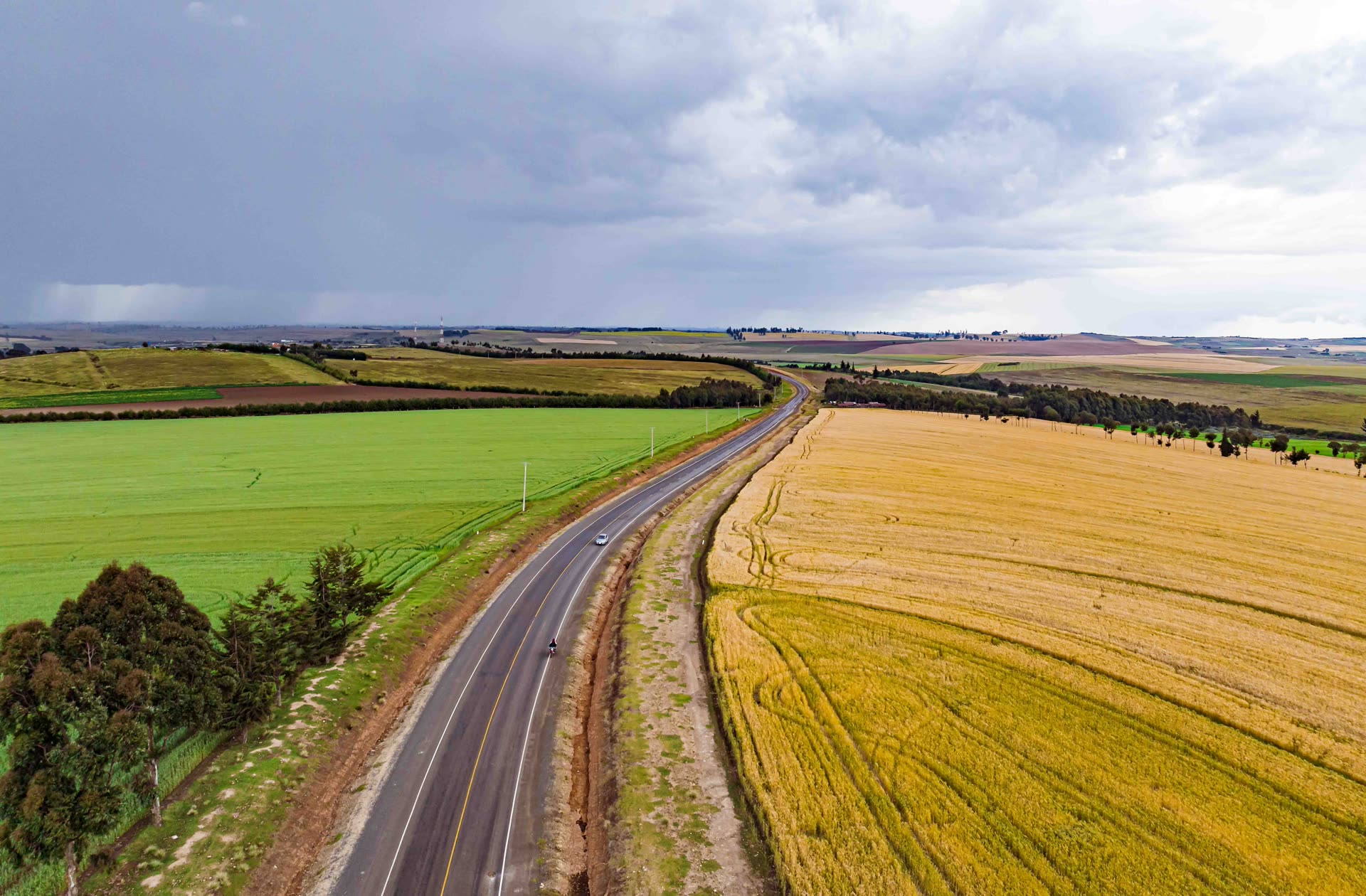 A two-lane highway running between green and golden wheat fields under a cloudy sky