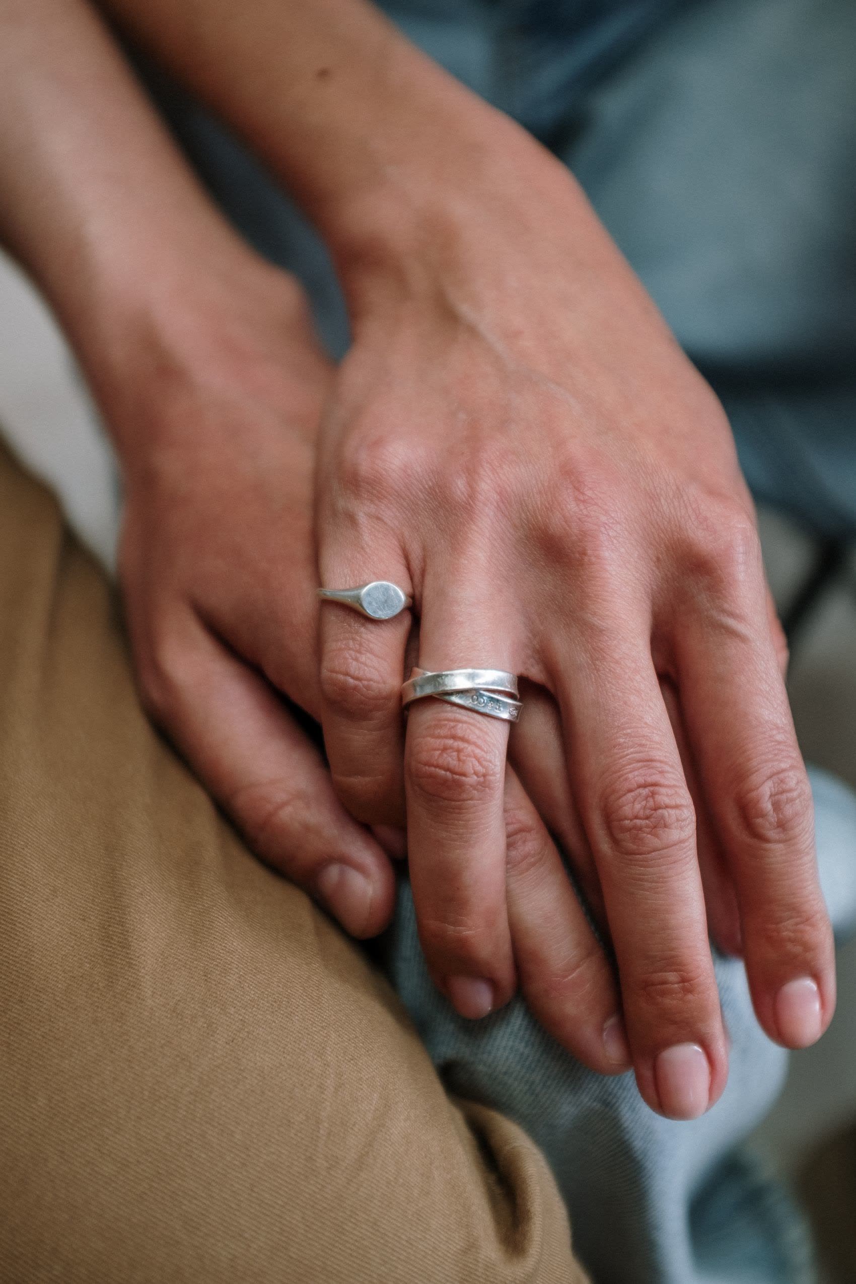 A hand wearing two plain silver rings resting on a knee