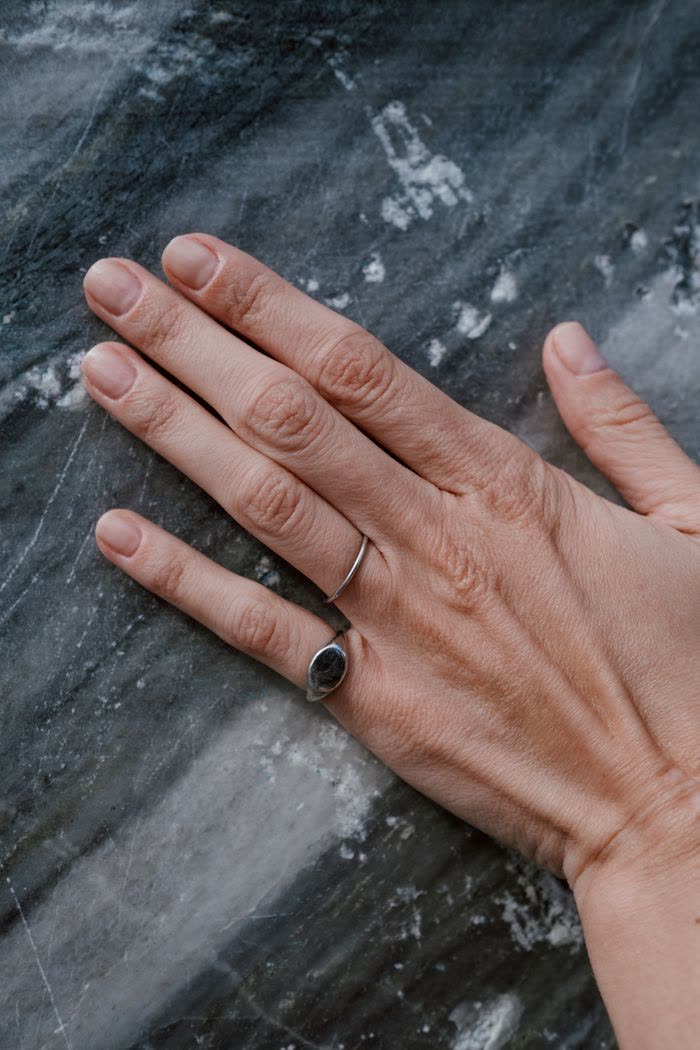 A hand resting on dark marble wearing a thin band