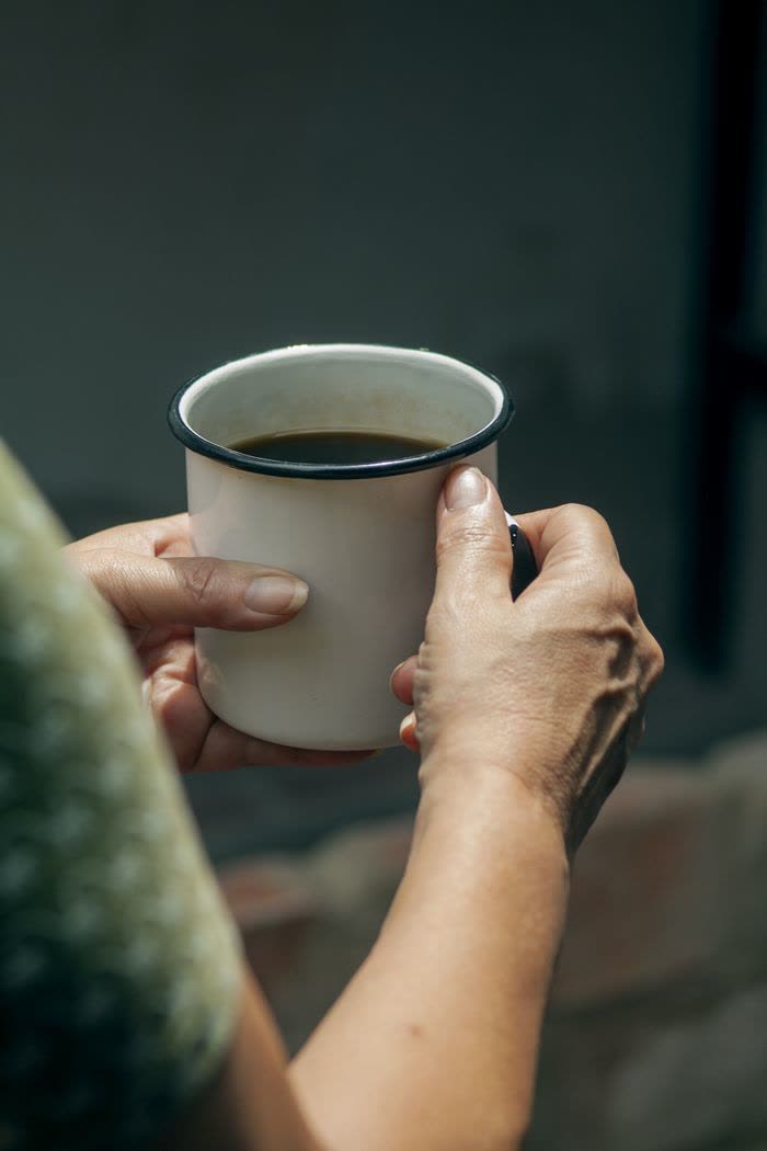Two hands holding an enamel coffee cup