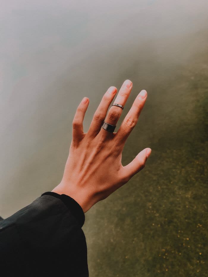 A raised hand wearing a plain band ring against fog