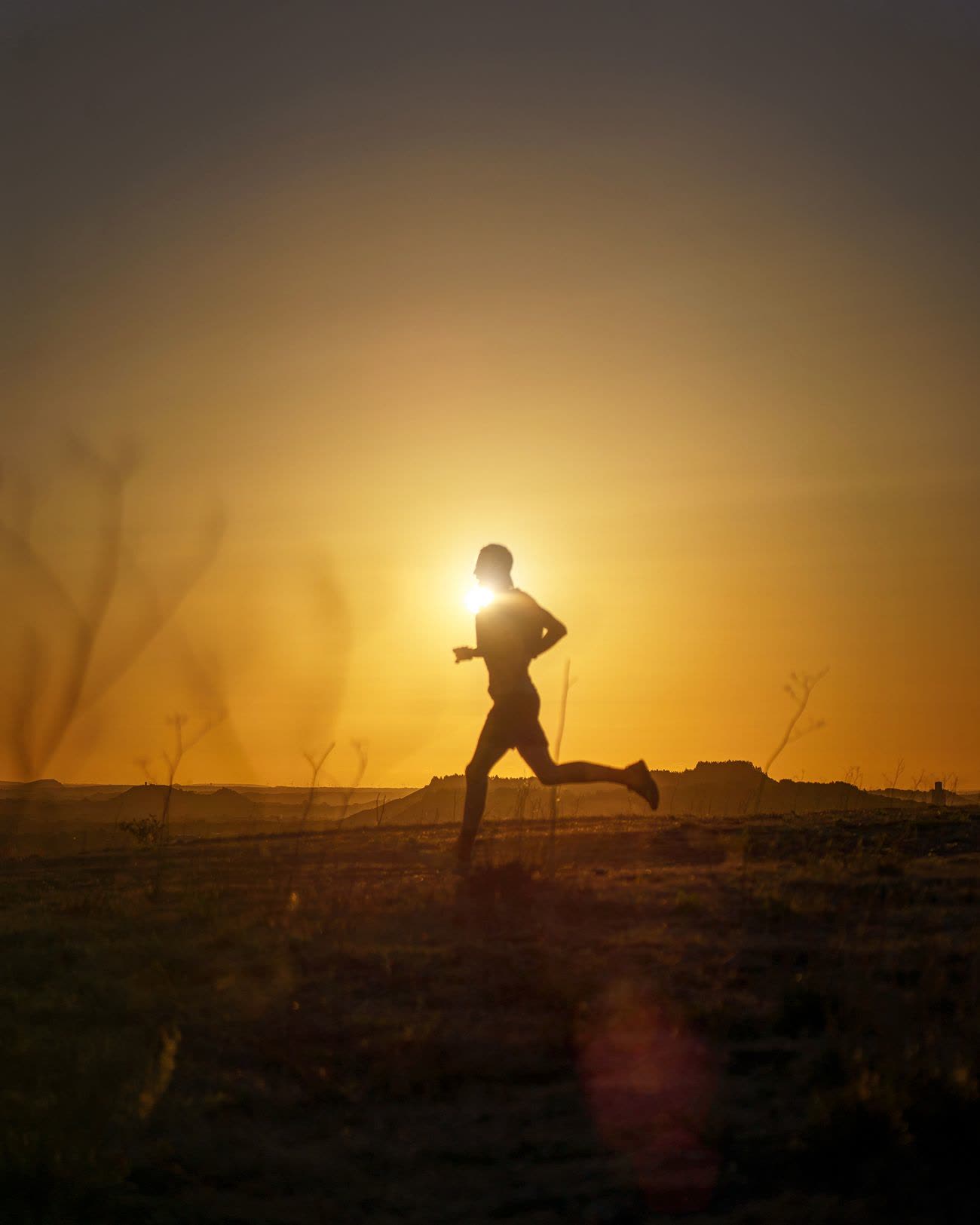 A runner silhouetted against a low orange sun