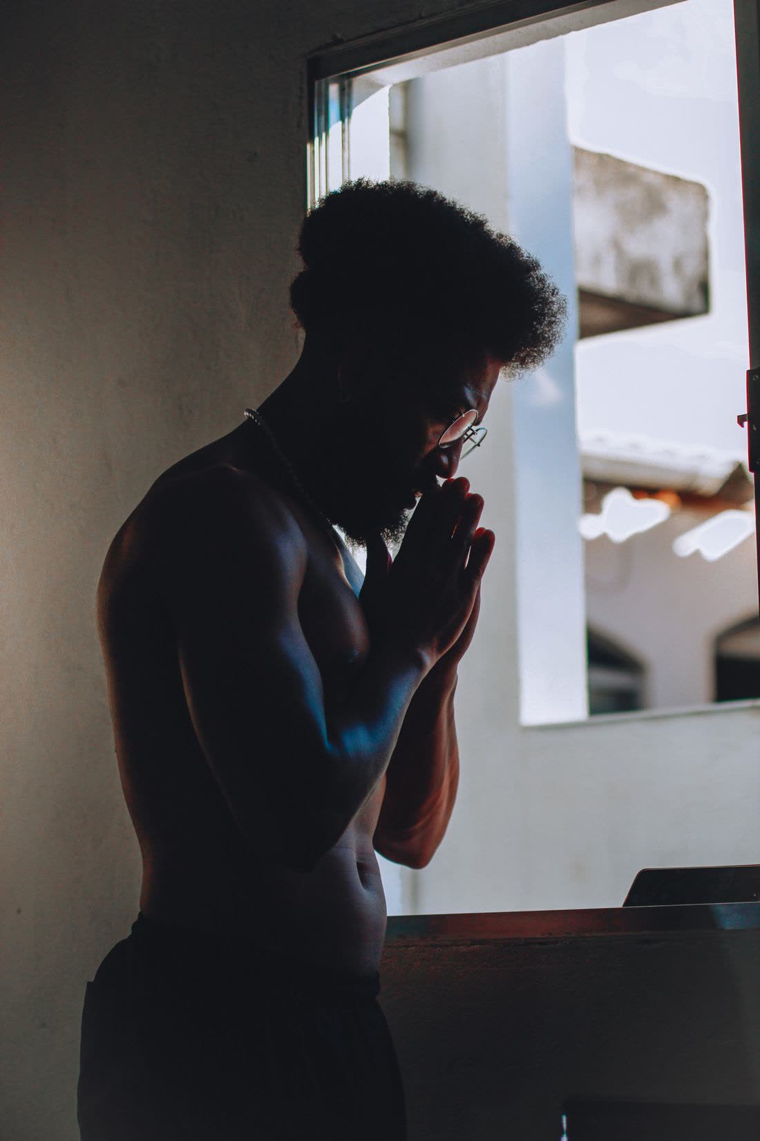 A man standing by a window with his hands pressed together