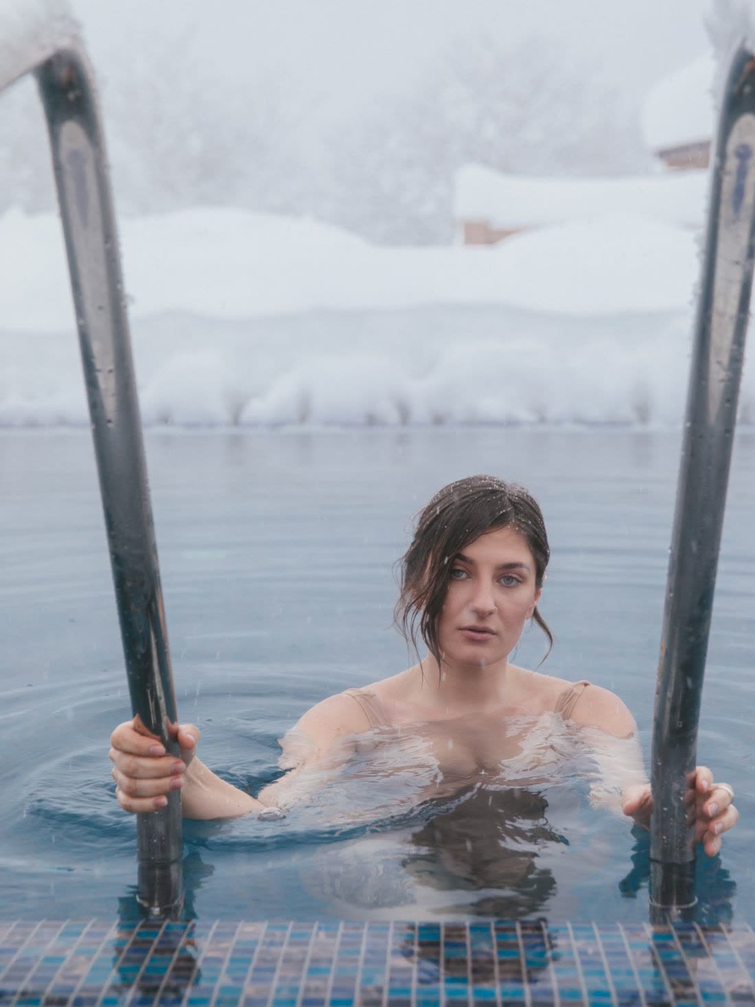 A woman holding the ladder of a cold outdoor pool in snow