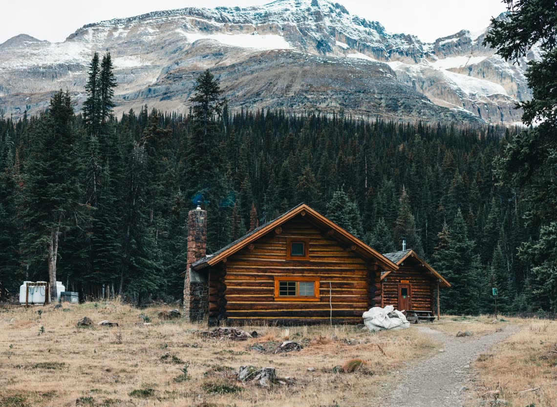 Log cabin among spruce below a snow-dusted mountain face