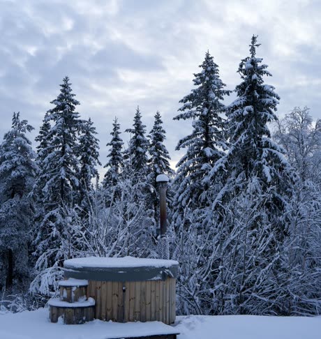 Covered wooden soaking tub in fresh snow under spruce trees