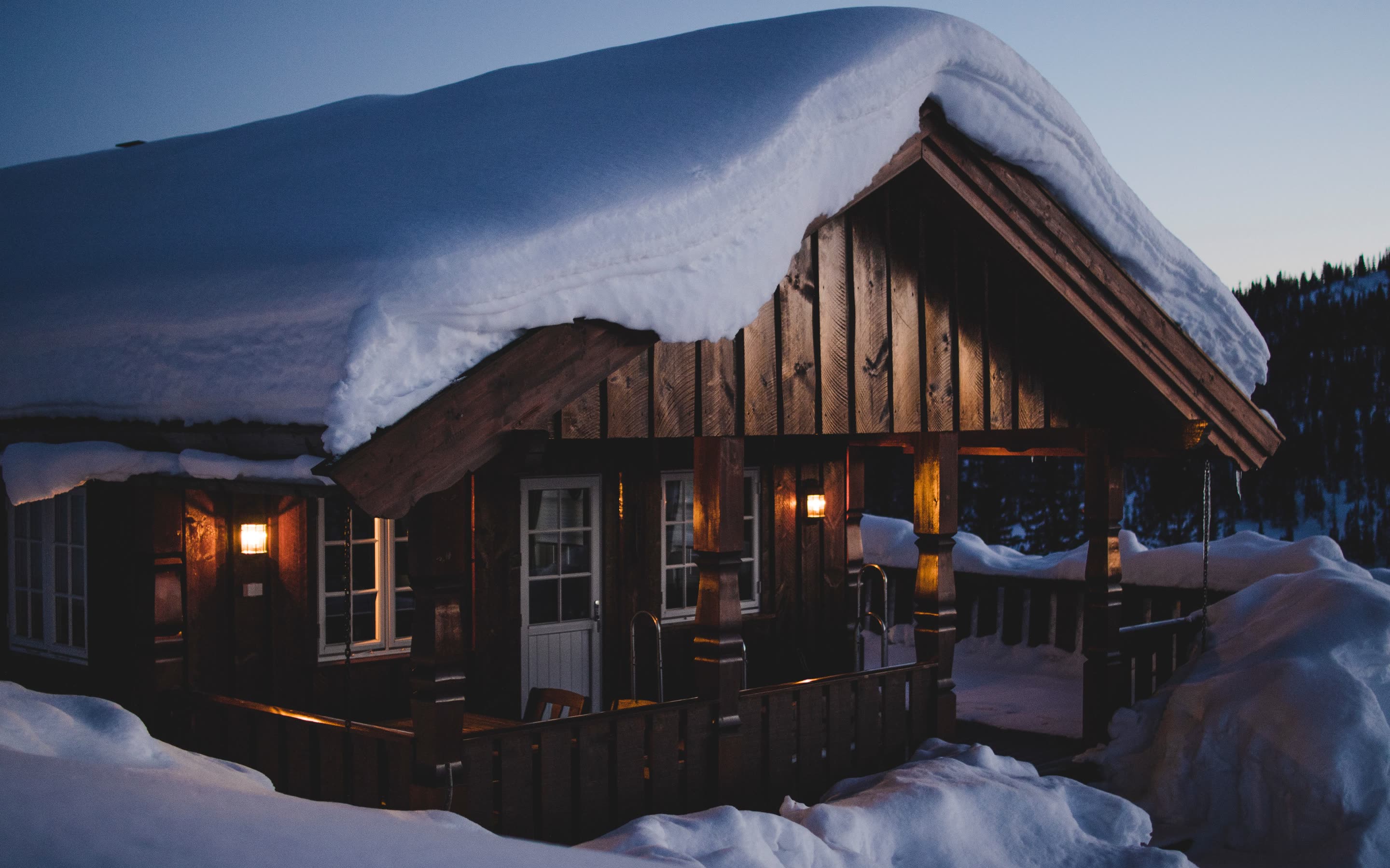 Snow-loaded log lodge porch lit at dusk