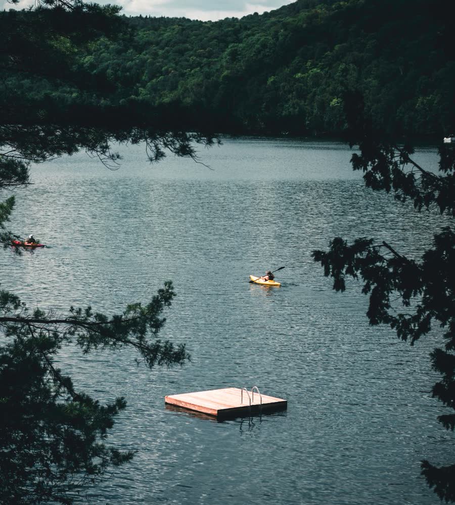 A kayaker crossing a forested lake past a swim float
