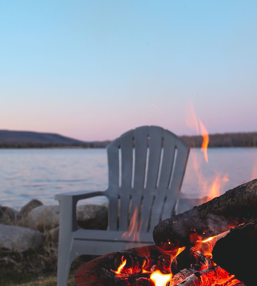 A lakeside fire with an Adirondack chair at dusk