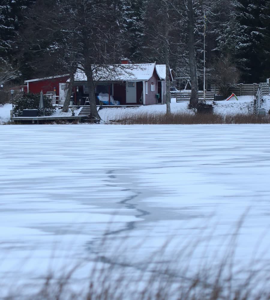 A frozen lake in front of a snowy lakeside cabin