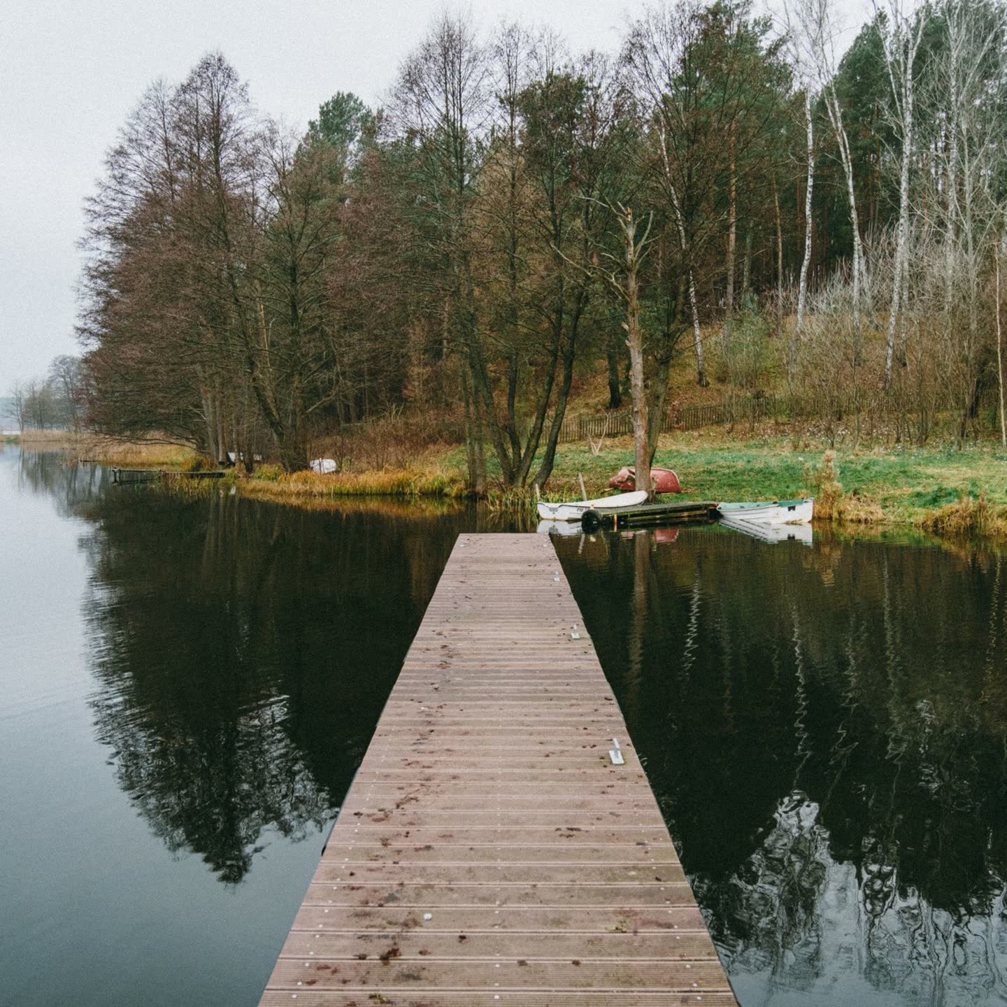 A wooden pier running out into a still lake lined with autumn trees