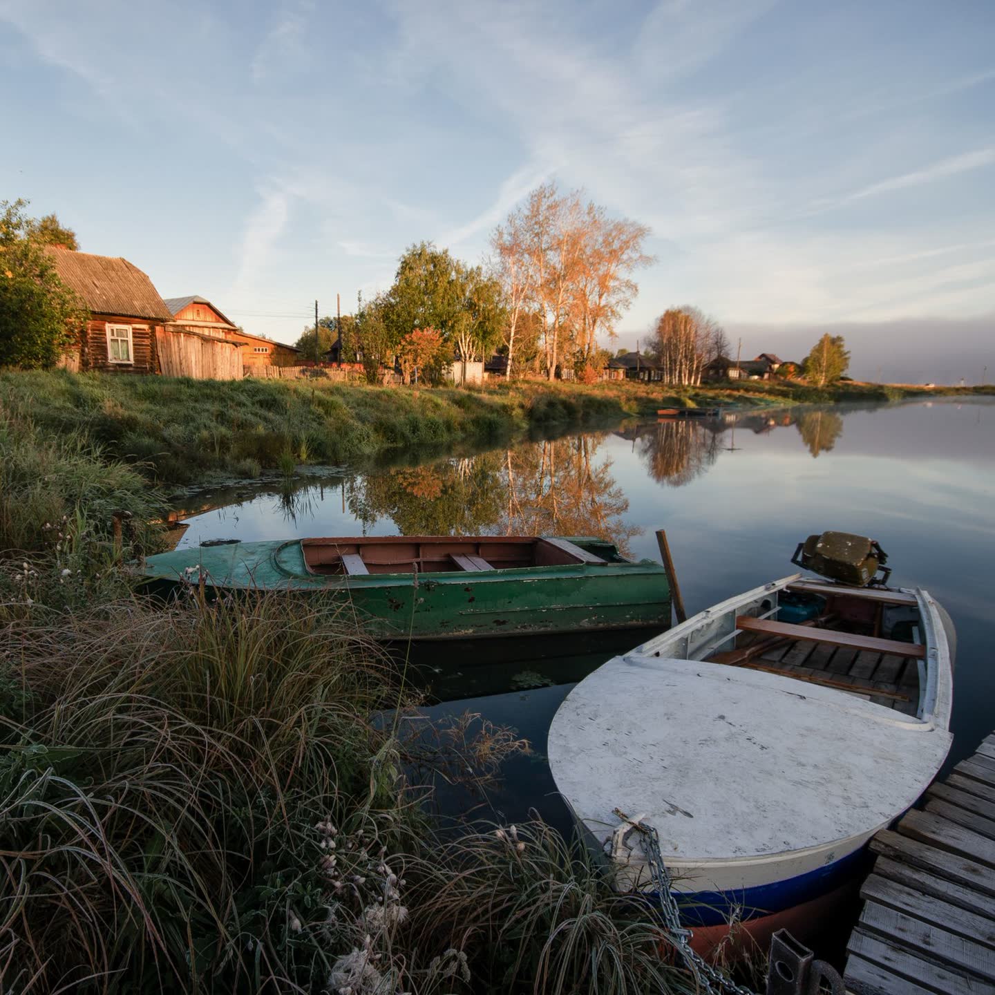 Two small boats pulled up on a grassy lakeshore at golden hour