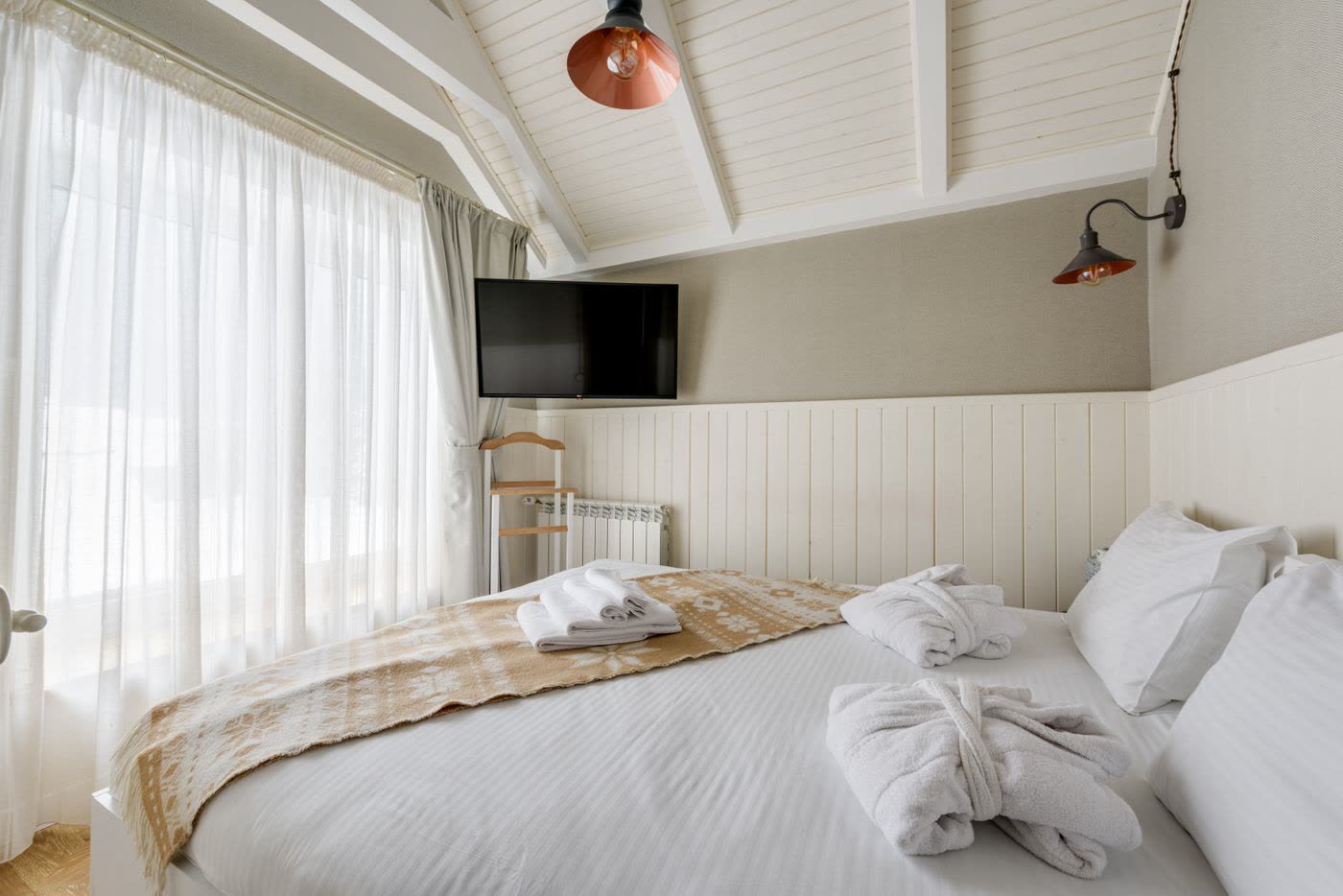Guest room with a white bed, robes and a vaulted plank ceiling