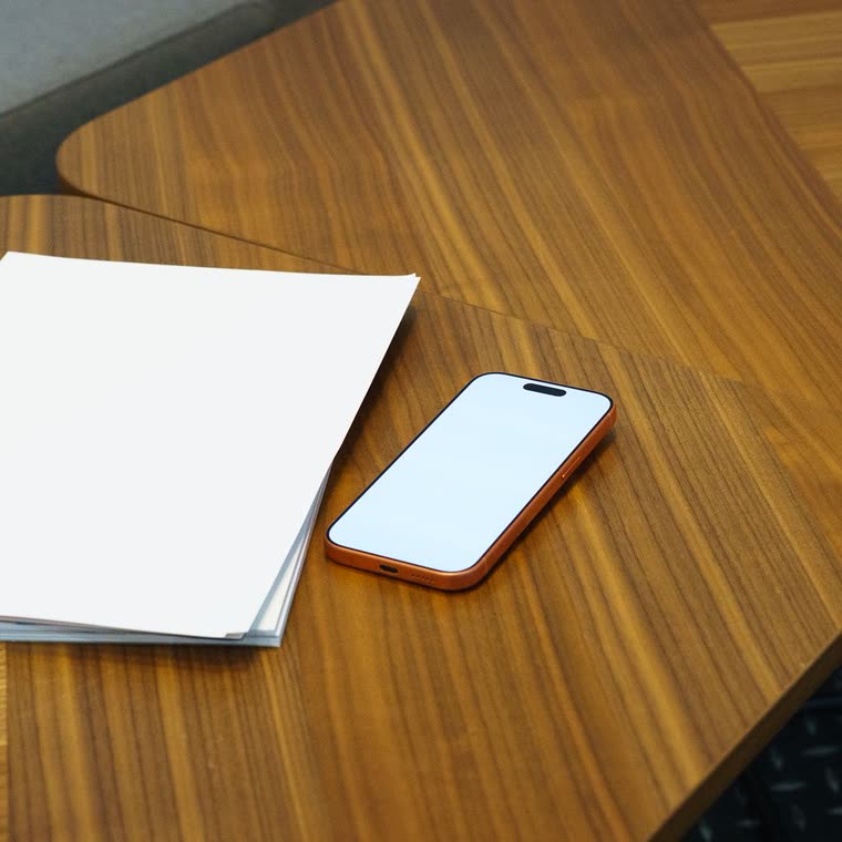 A phone and a stack of paper on a wooden table