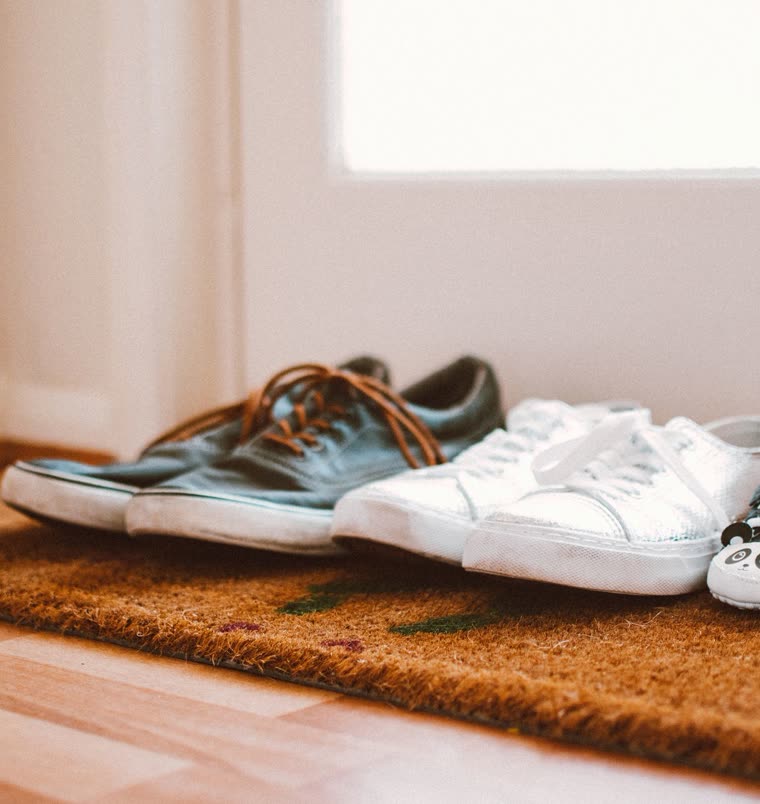 Three pairs of shoes on a doormat, one of them small