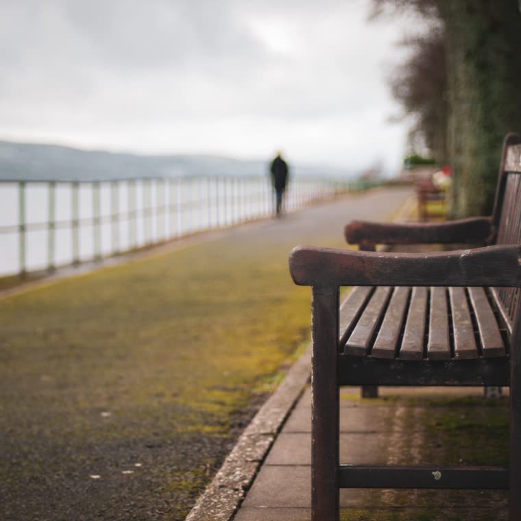 A bench on a lakeside path under grey sky