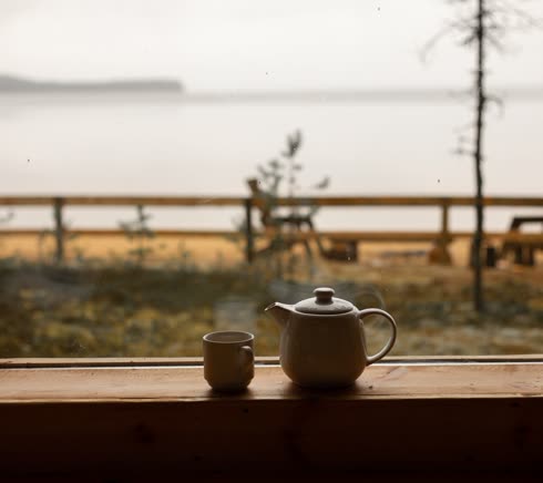 A teapot and a cup on a window ledge looking out to the water