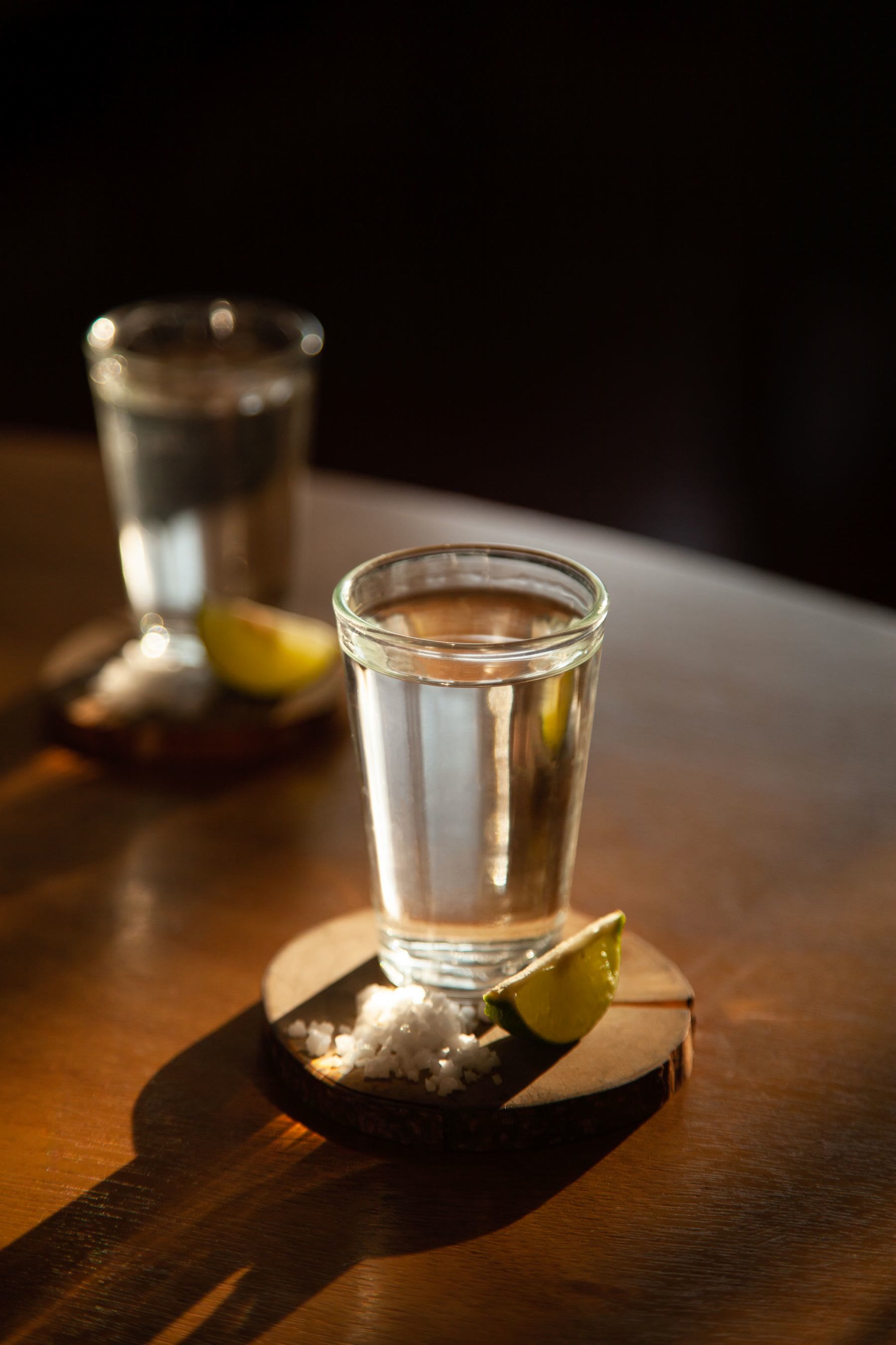 A pour of clear agave spirit with lime and salt on a wooden bar