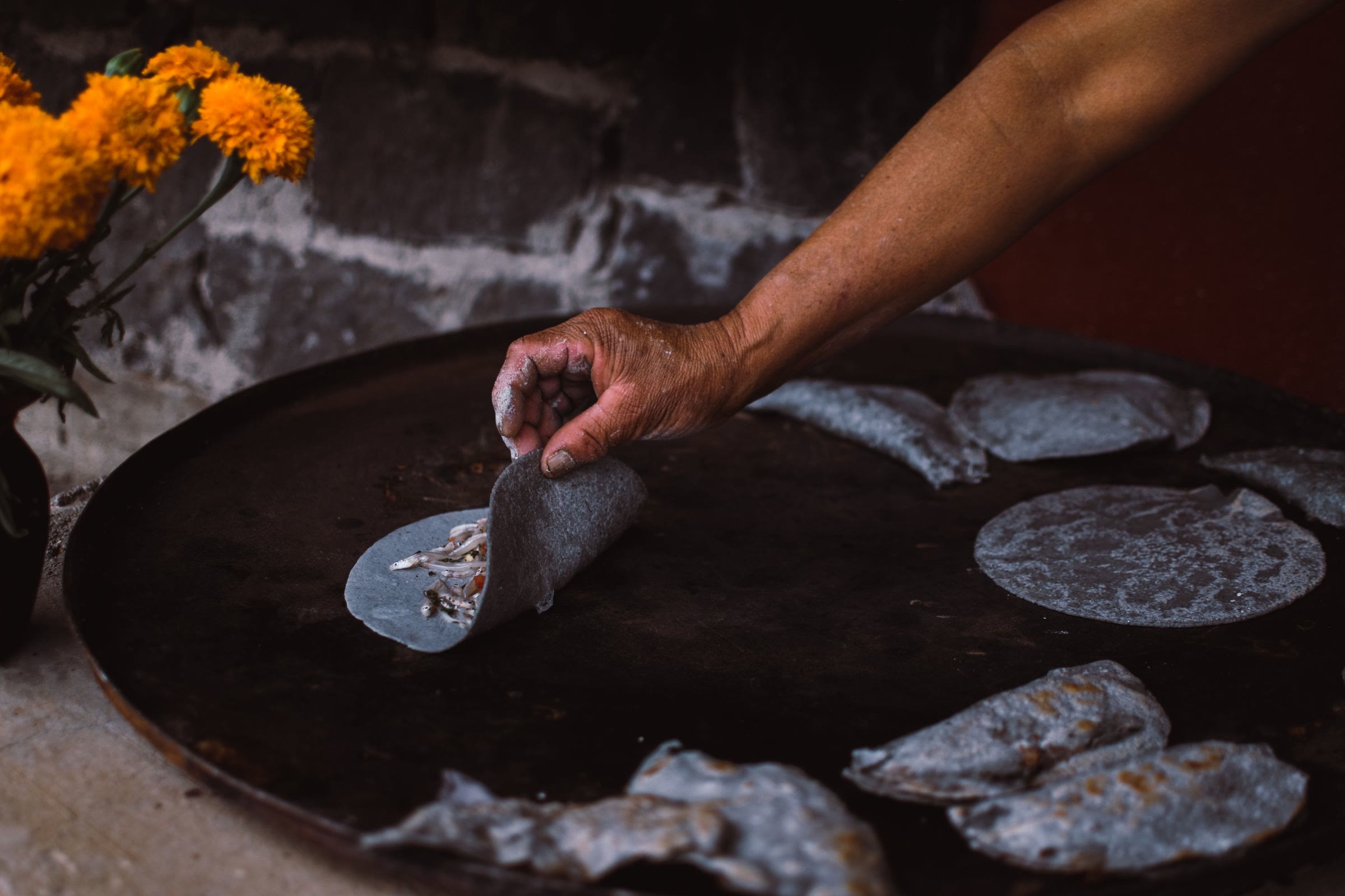 A hand turning blue corn masa on a wide black comal