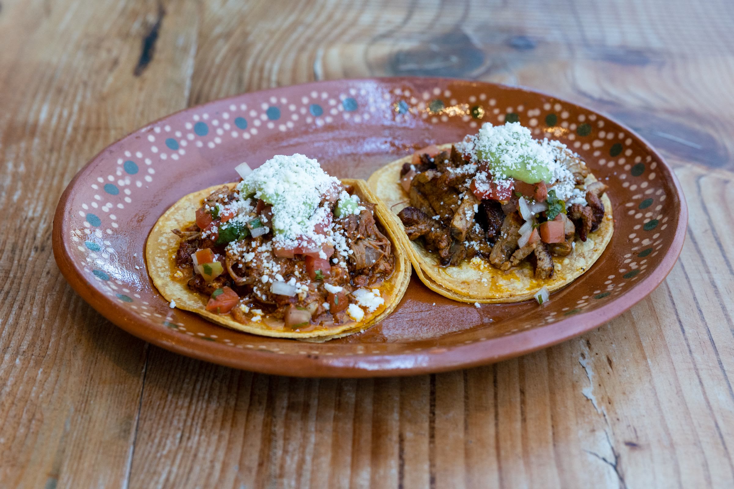 Two tacos with queso fresco on a painted clay plate