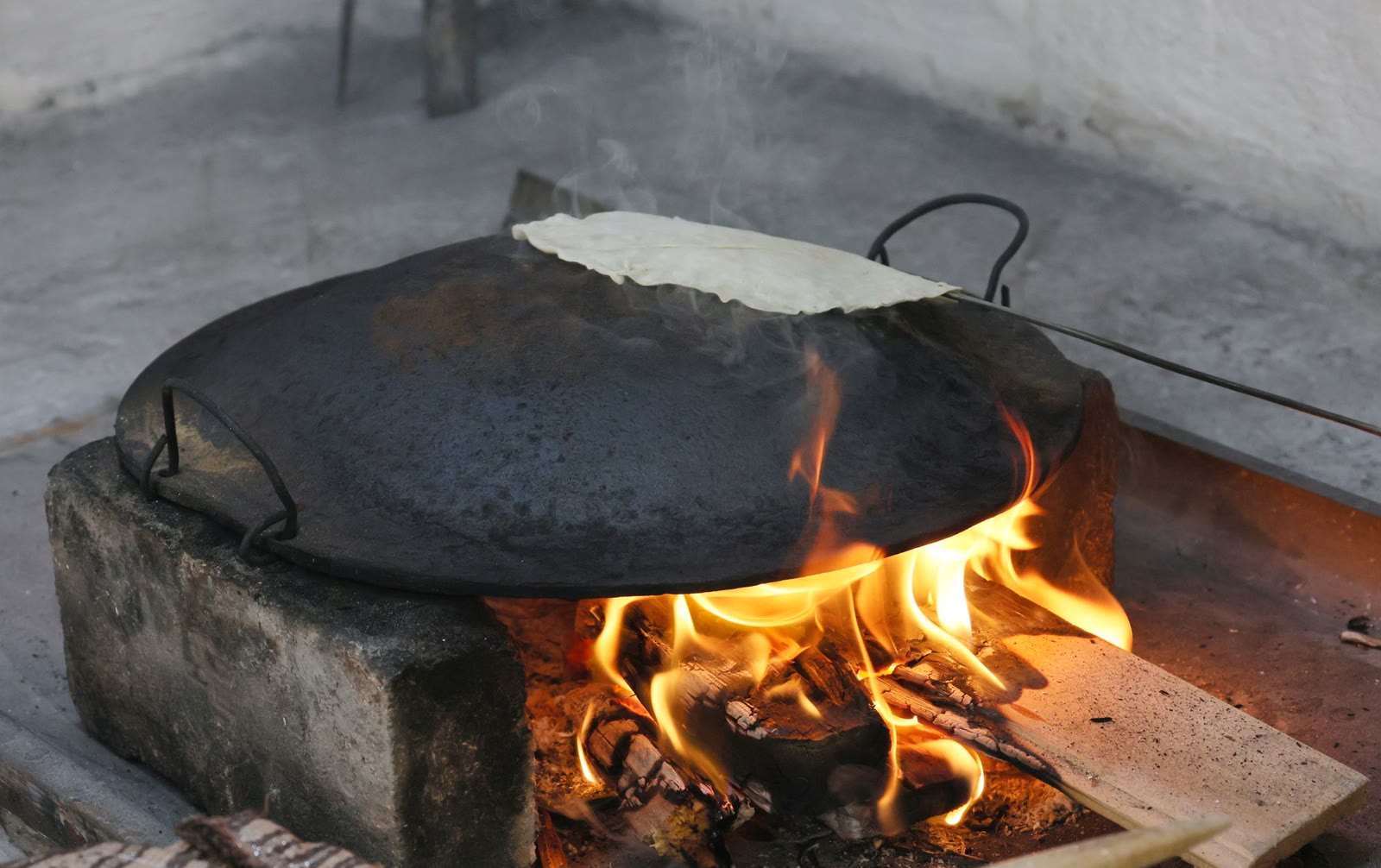 A tortilla on a comal resting over a wood fire