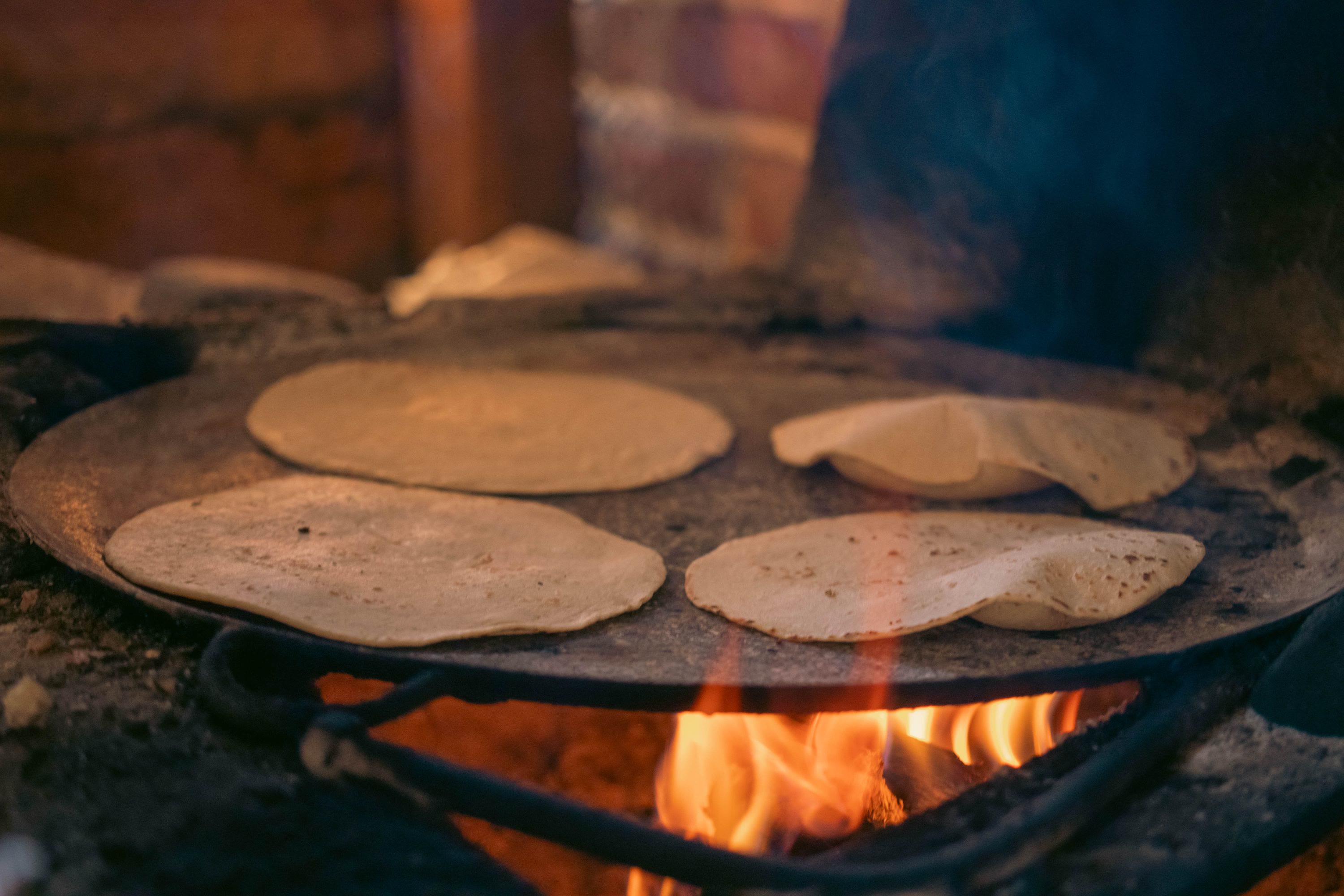 Corn tortillas puffing on a wide comal over an open wood fire