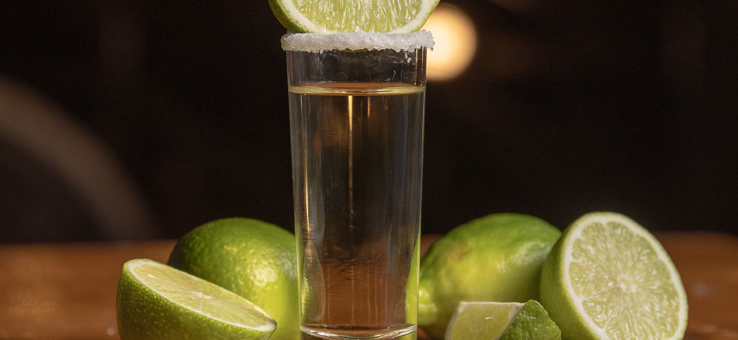 A pour of blanco with lime wedges on the bar top