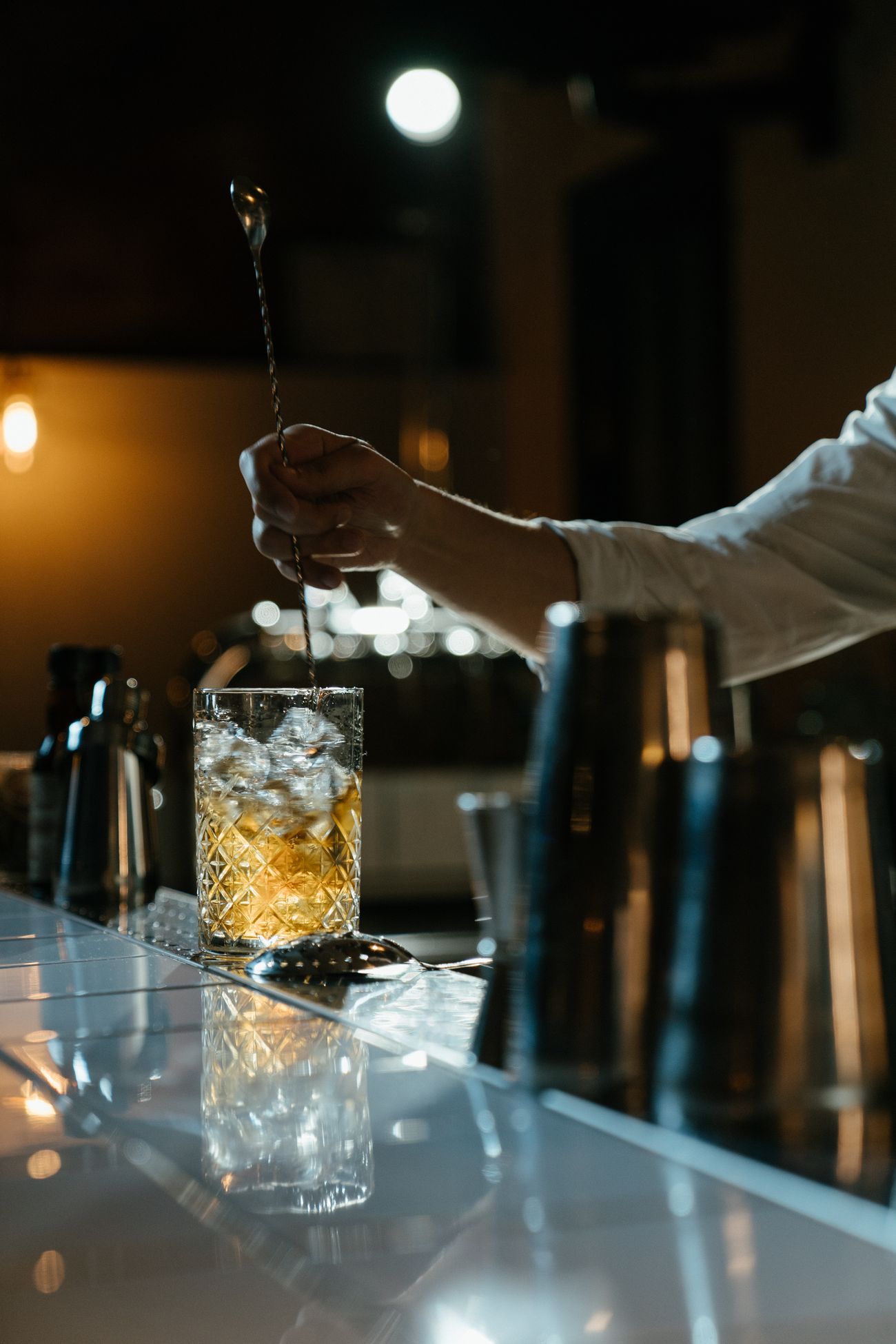 A bartender stirring a whiskey cocktail in a cut-glass mixing glass