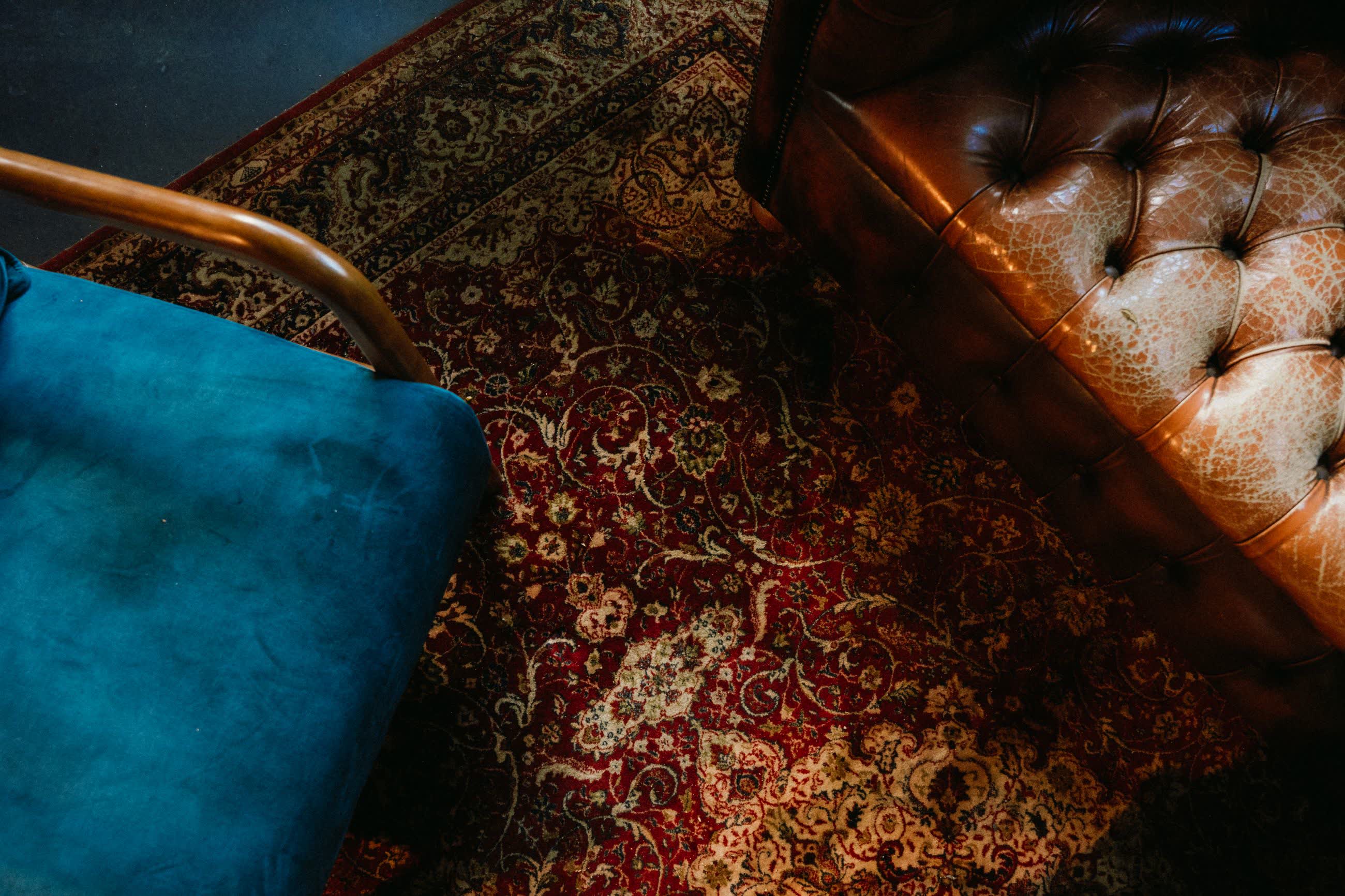 A teal velvet armchair, a tufted leather sofa and a red patterned rug seen from above