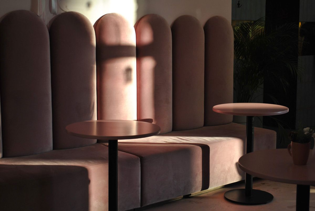 Rounded blush velvet booths and small pedestal tables in low light