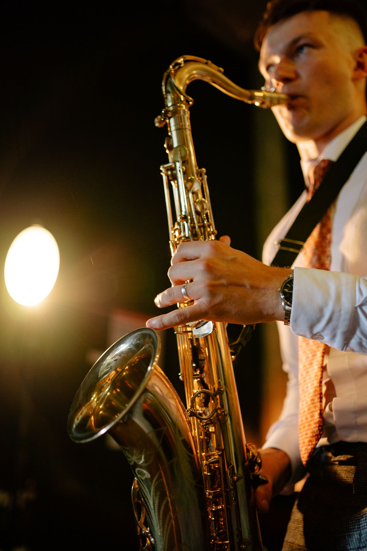 A saxophonist in a white shirt and tie playing under a warm stage light
