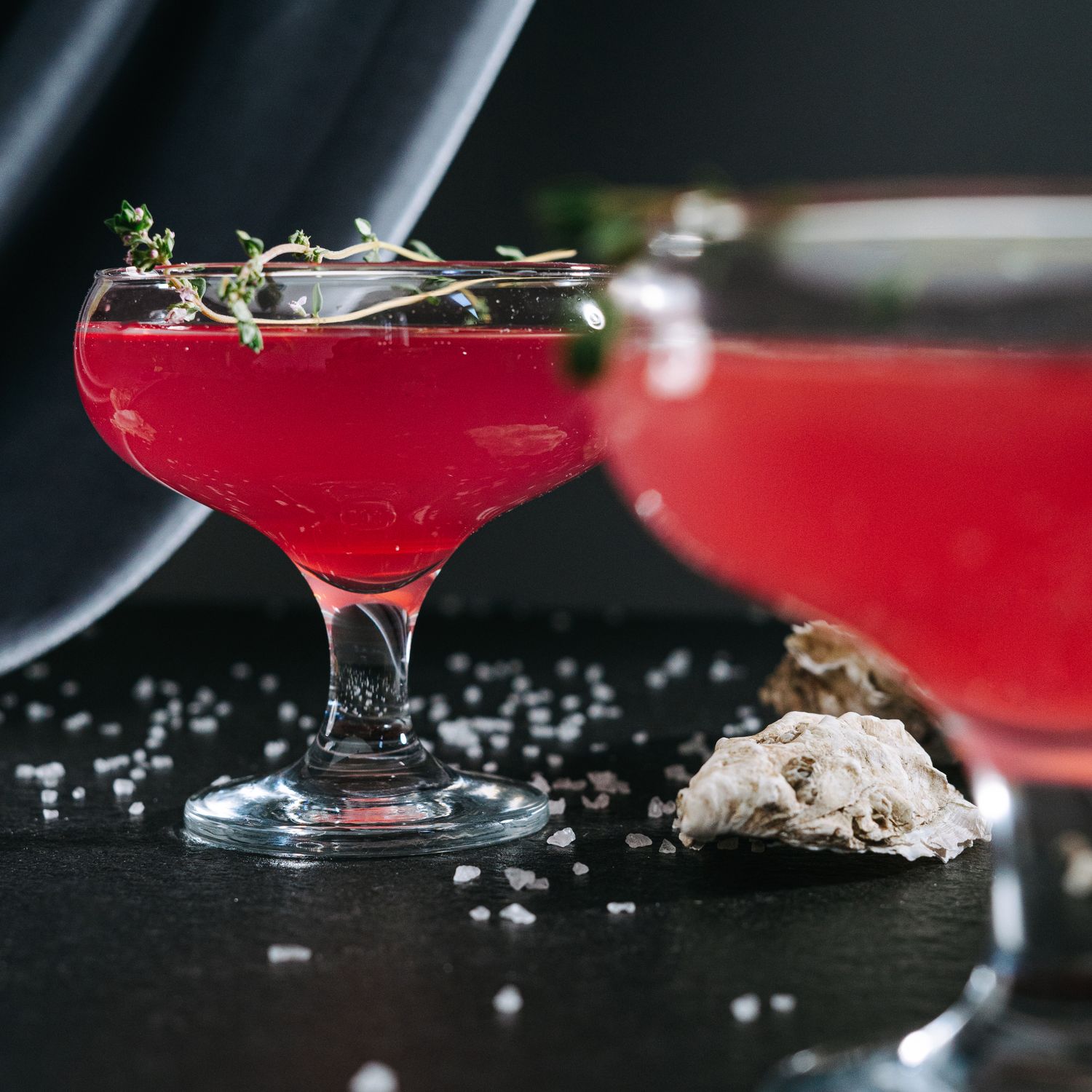 Two red coupe cocktails garnished with thyme on a dark slate table