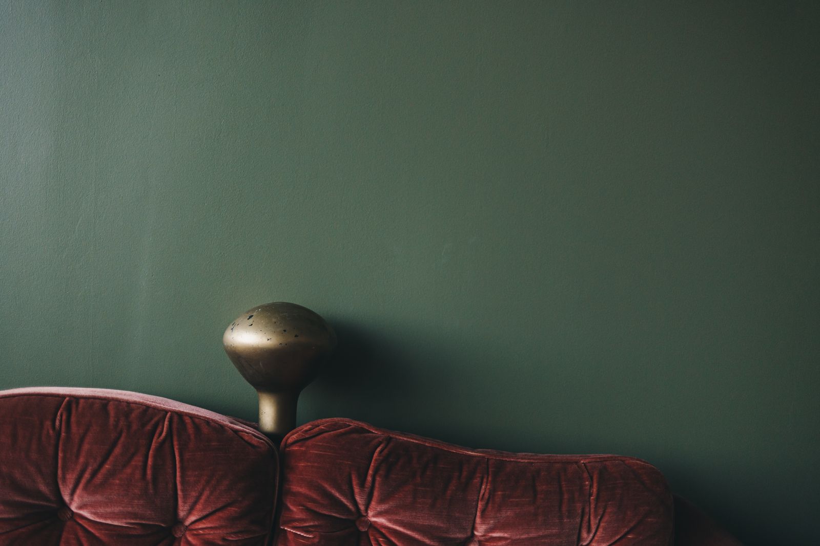 The rolled back of a rose velvet sofa against a dark green wall